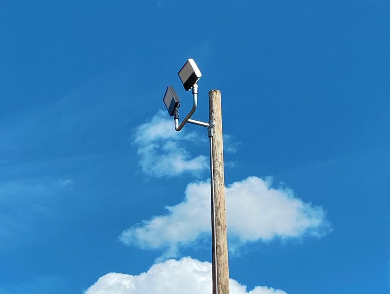 Wooden utility pole with two mounted security lights against a blue sky with clouds.